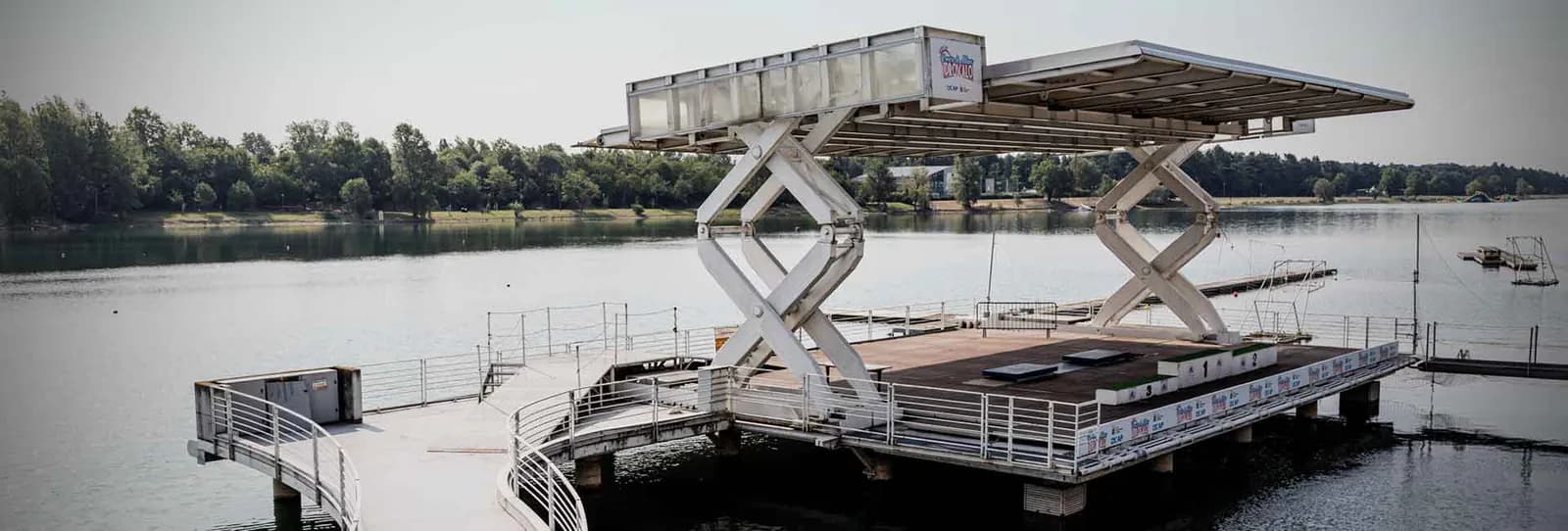 Širok pogled na podignutu metalnu platformu iznad vode na Idroscalu, s ogradama i drvećem u pozadini.