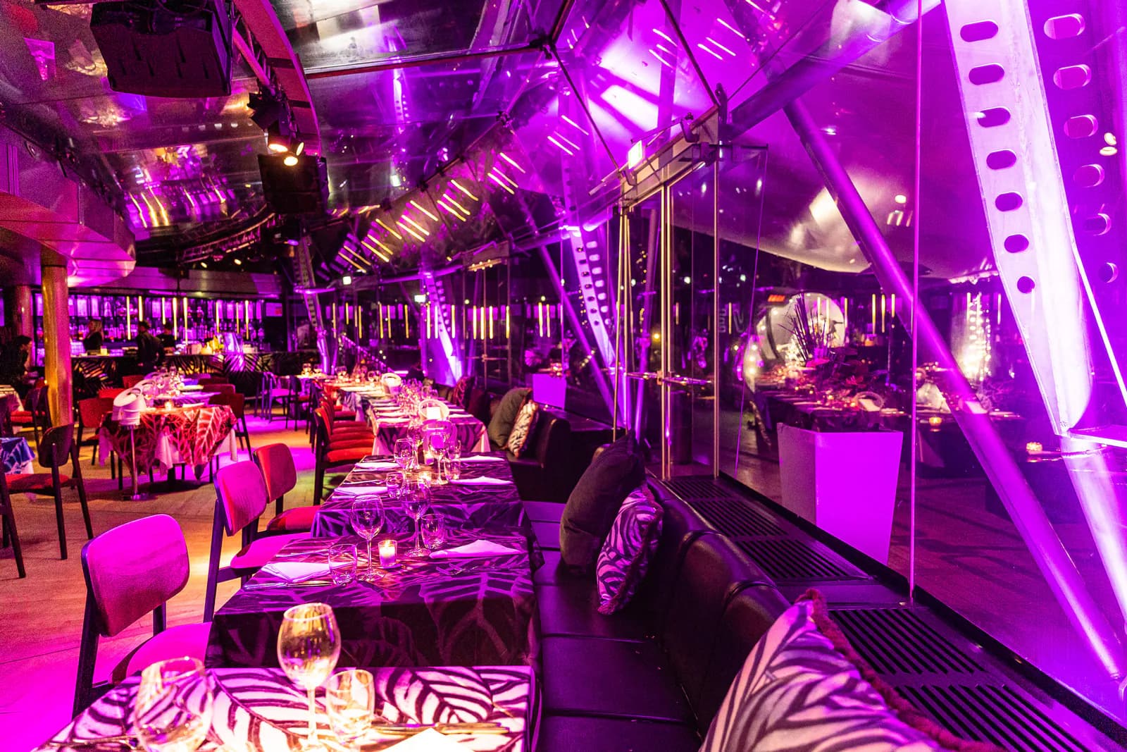 Restaurace s prostřenými stoly, skleněnými stěnami a fialovým světlem
