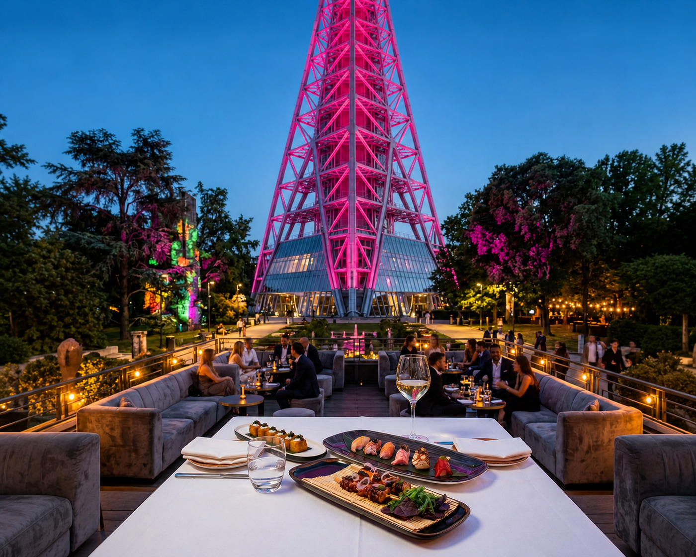 Outdoor lounge with guests, sofas and a laid table in front of Torre Branca lit in pink